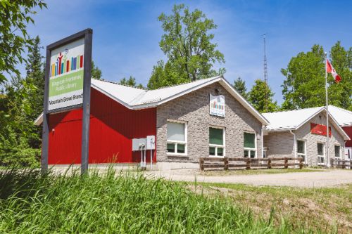 Small stone building with red siding and Mountain Grove sign 