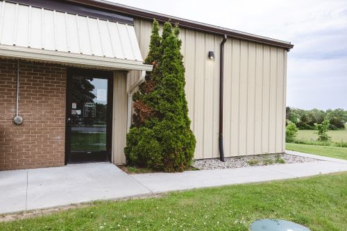 Main entrance to the branch in a brock and metal building with a large green cedar in the front. 