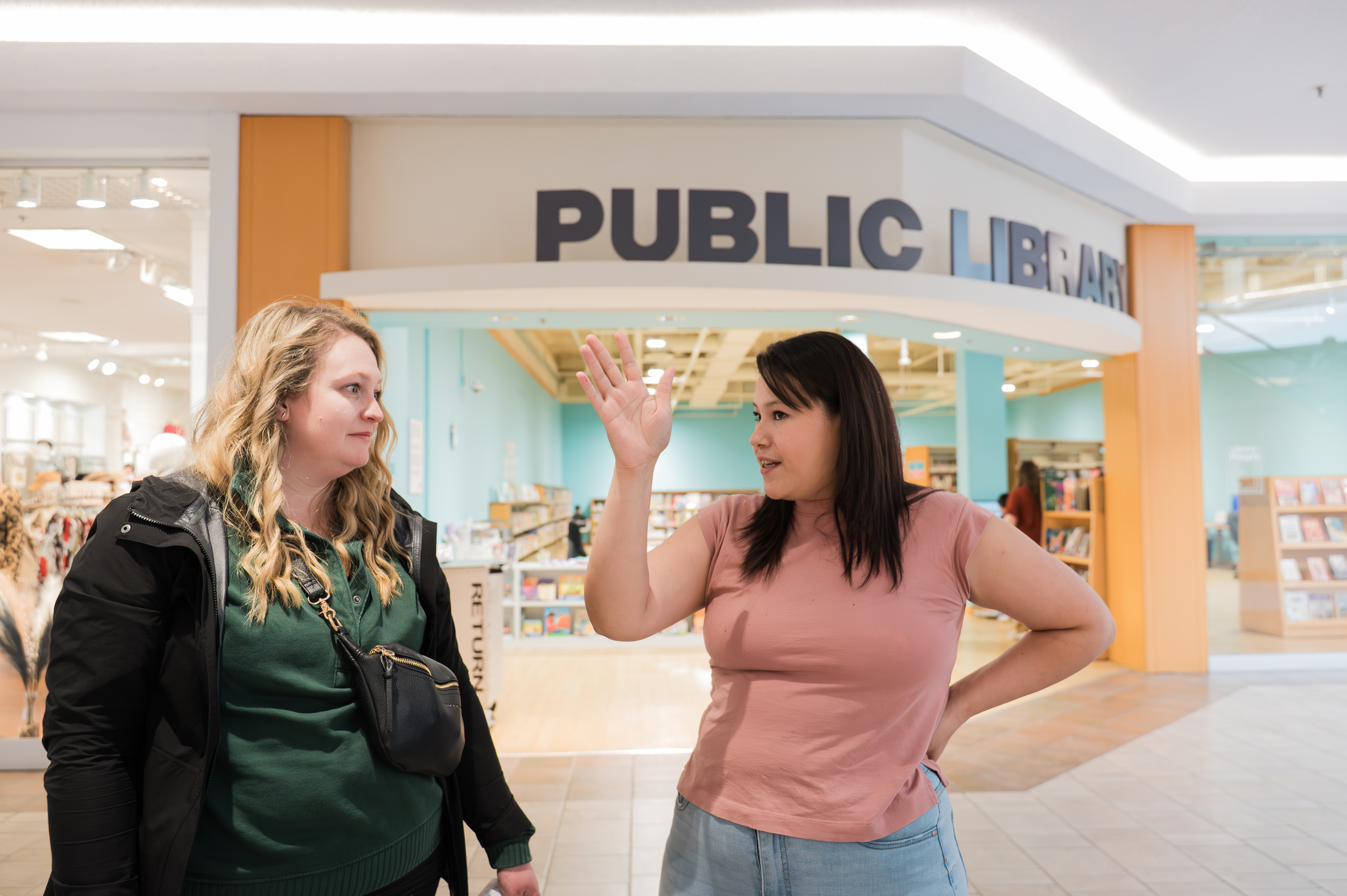 two women talking in front of the entrance to the library branch at the mall