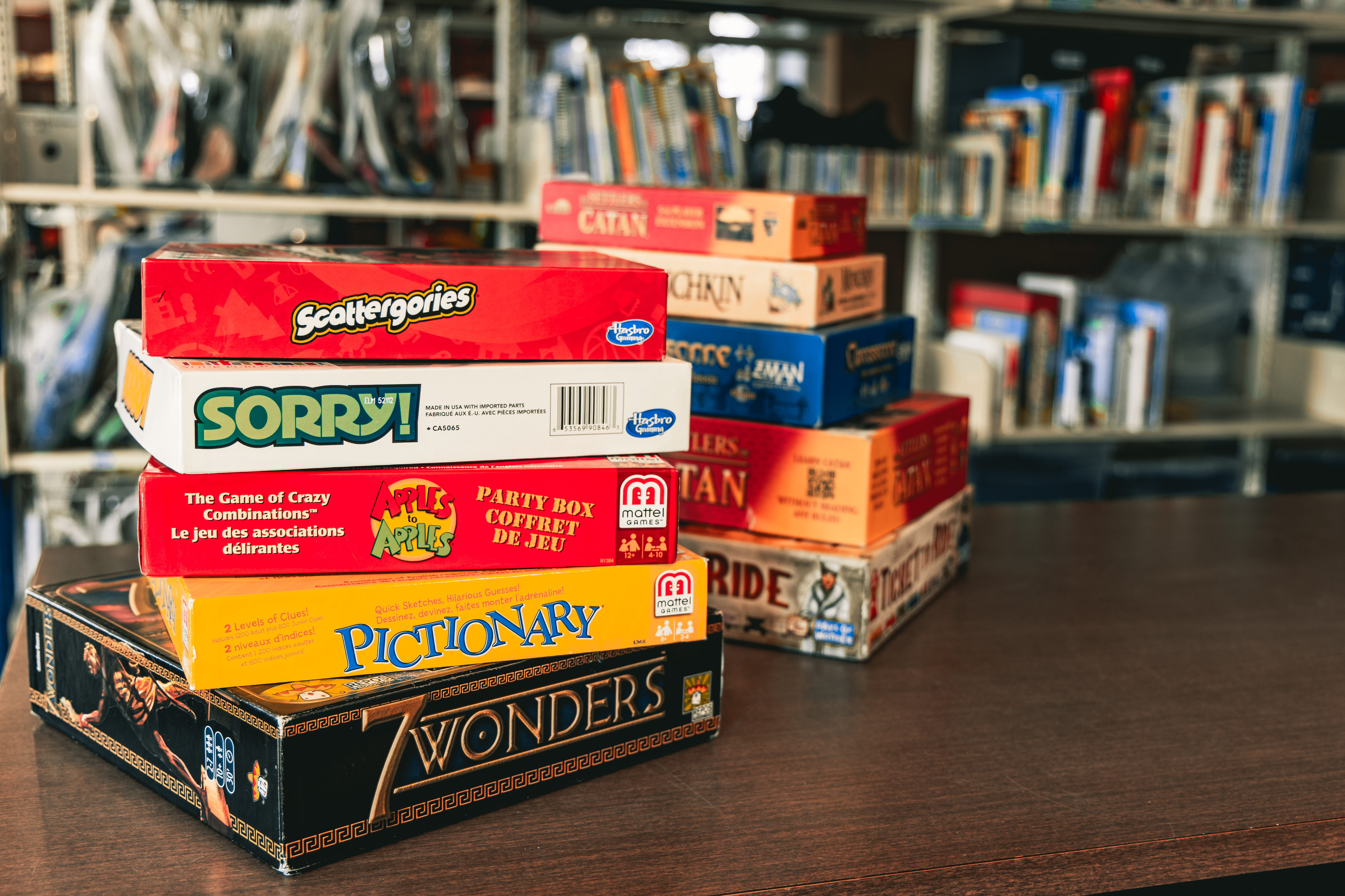 Two piles of board games with library shelves in the background.