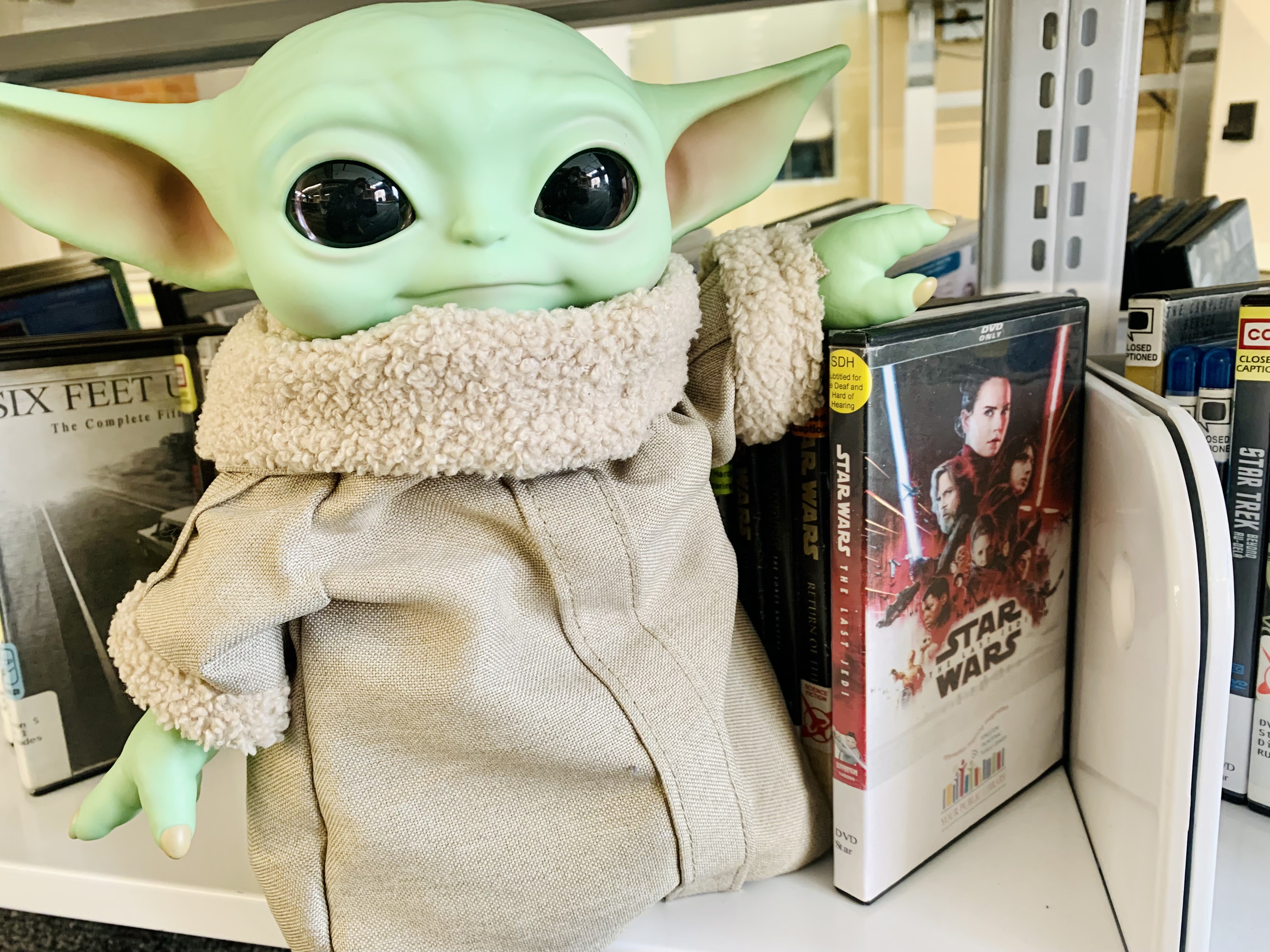 Grogu with a Star Wars DVD on a library shelf.