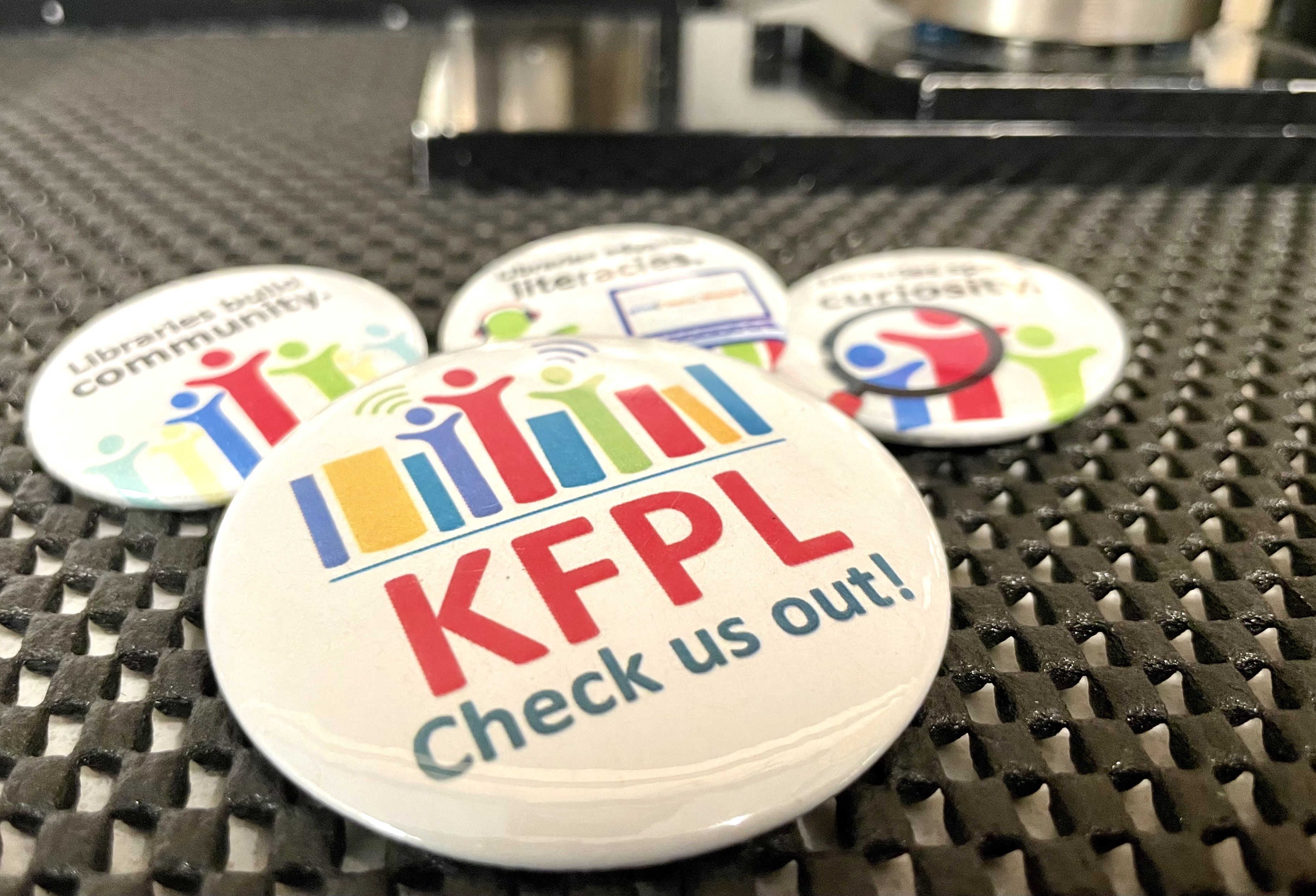 KFPL-themed buttons with button makers somewhat visible in the background.